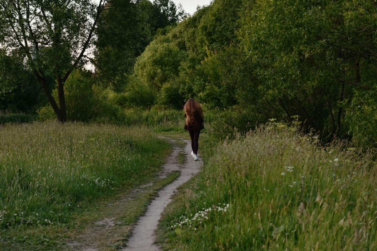 Kvinde går alene ad en smal sti gennem en grøn skov