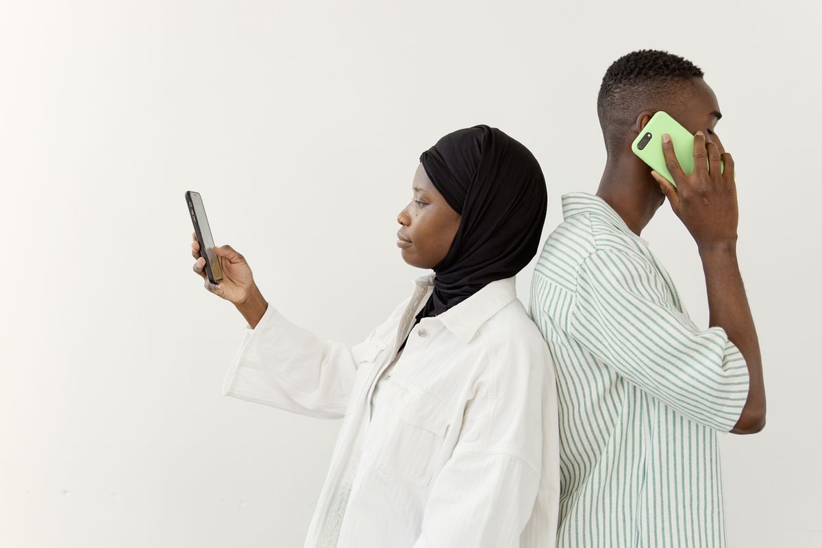 Et par står ryg mod ryg og kigger hver på sin mobiltelefon