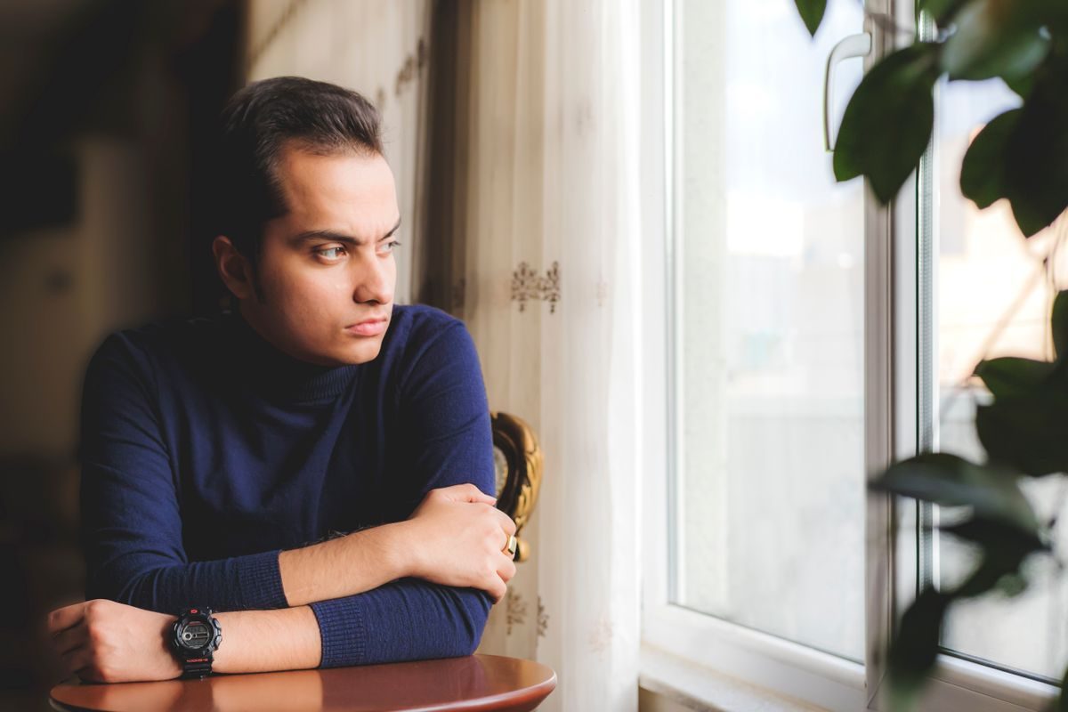 Mand i blå sweater sidder ved et vindue og kigger eftertænksomt ud