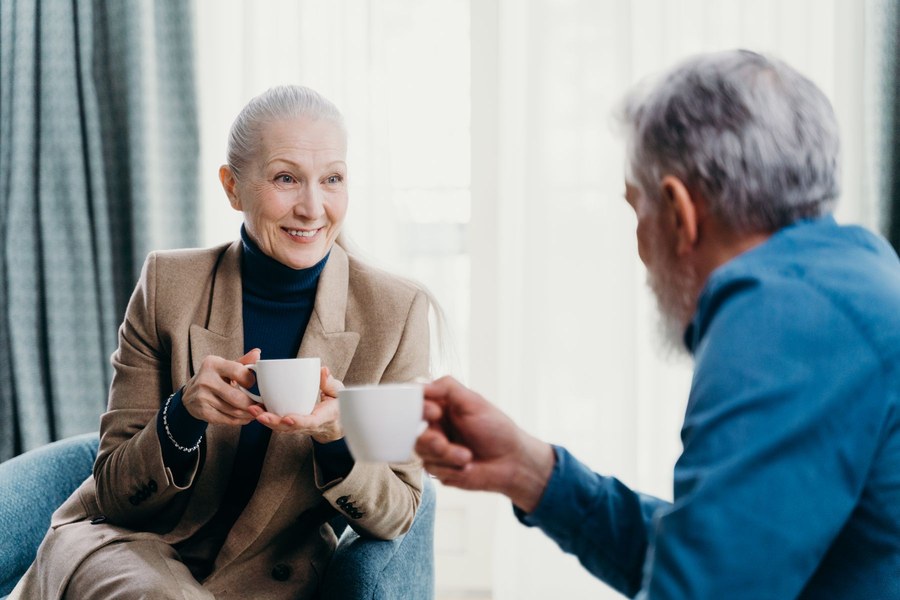 Gråhåret par sidder over for hinanden med en kop kaffe og taler roligt sammen