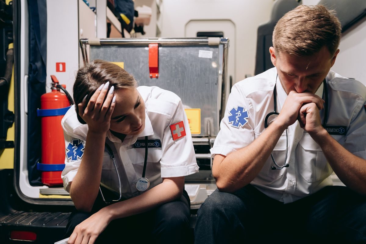 To ambulancefolk sidder bag i en ambulance og ser tyngede ud efter en opgave