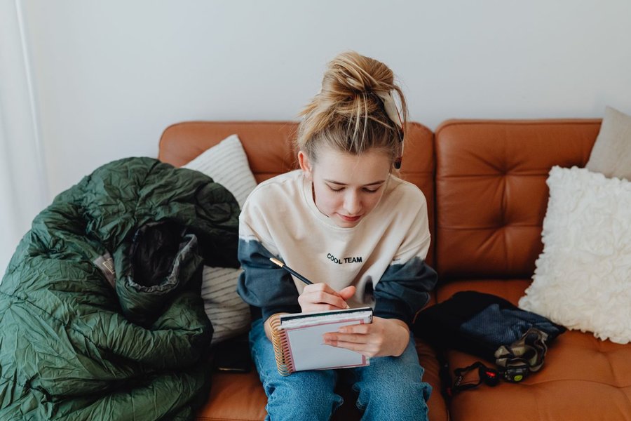 Ung kvinde med lyst hår sidder i en brun sofa og skriver i en notesbog