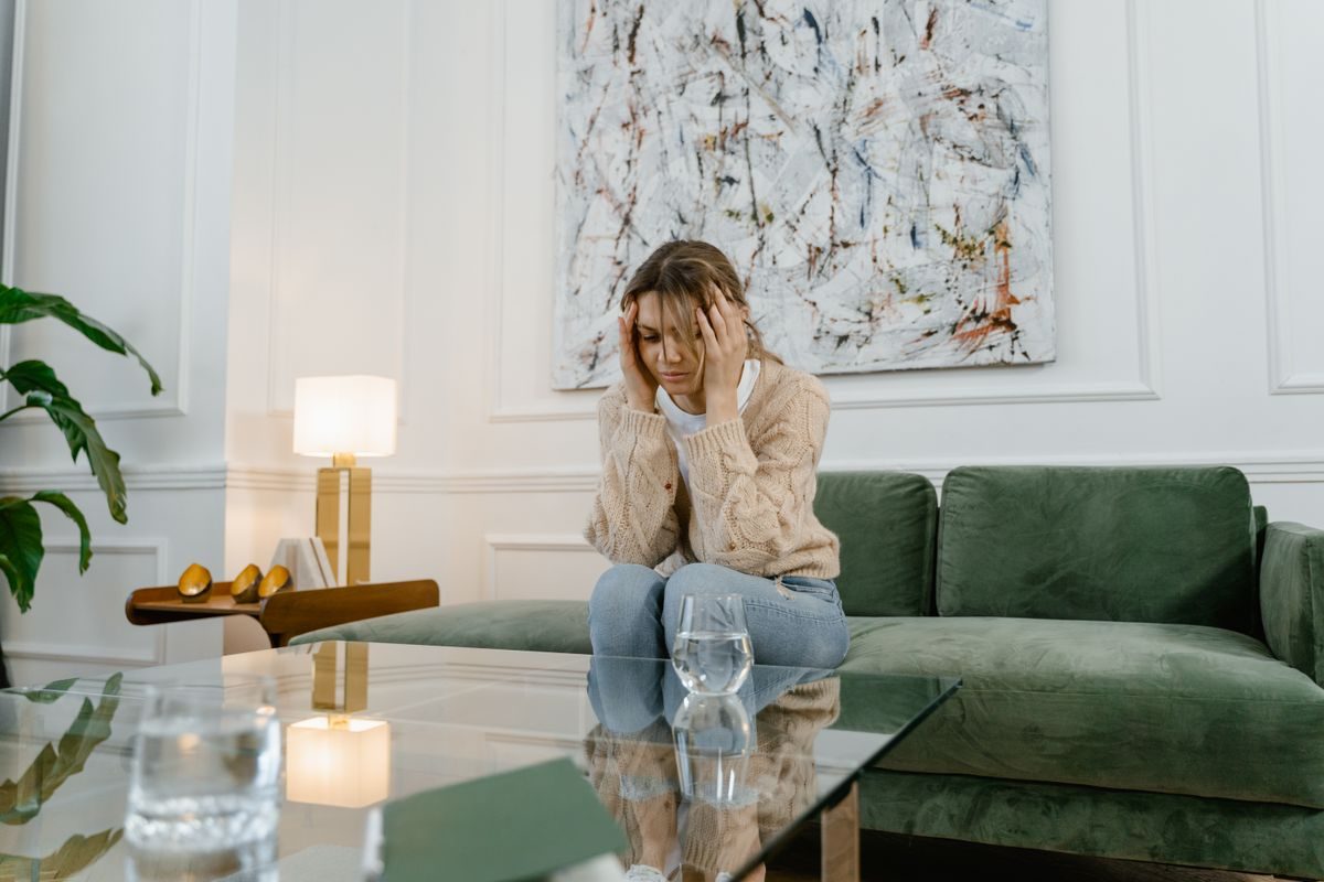 Kvinde sidder alene på en grøn sofa med hånden mod hovedet og ser bekymret ud
