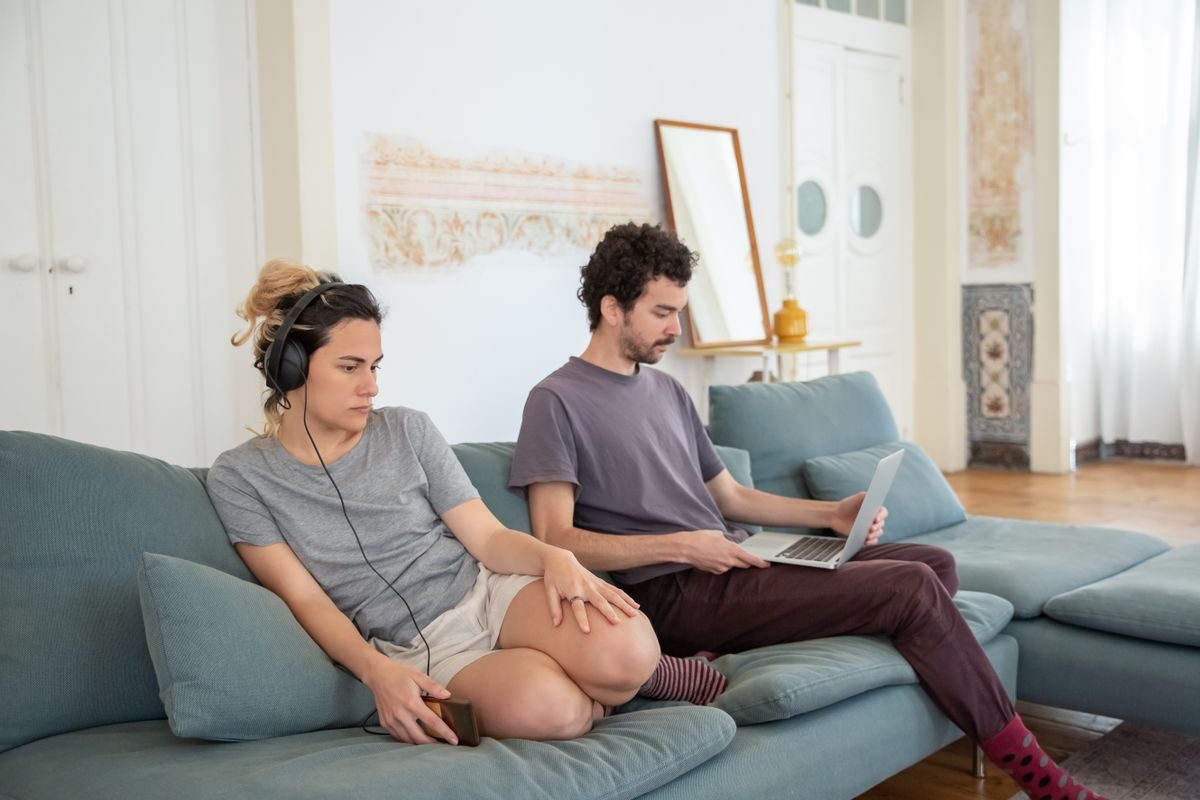 Kvinde med høretelefoner sidder i sofaen ved siden af en mand, der kigger på sin bærbare computer