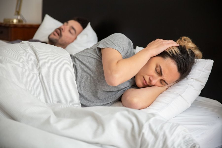 Kvinde ligger vågen i sengen og holder sig for hovedet, mens hendes partner sover