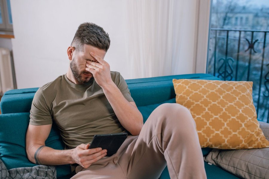 Mand sidder i en sofa med en tablet og holder hånden mod panden