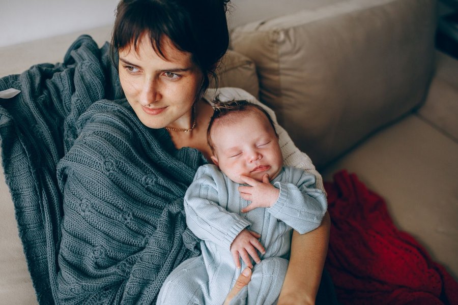 Mor sidder i en sofa under et tæppe med sin nyfødte baby i armene