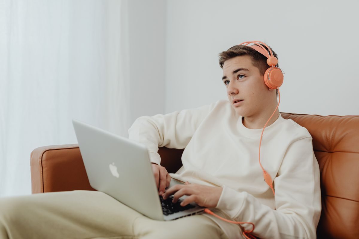 Teenagedreng med orange høretelefoner sidder i en sofa med en bærbar computer